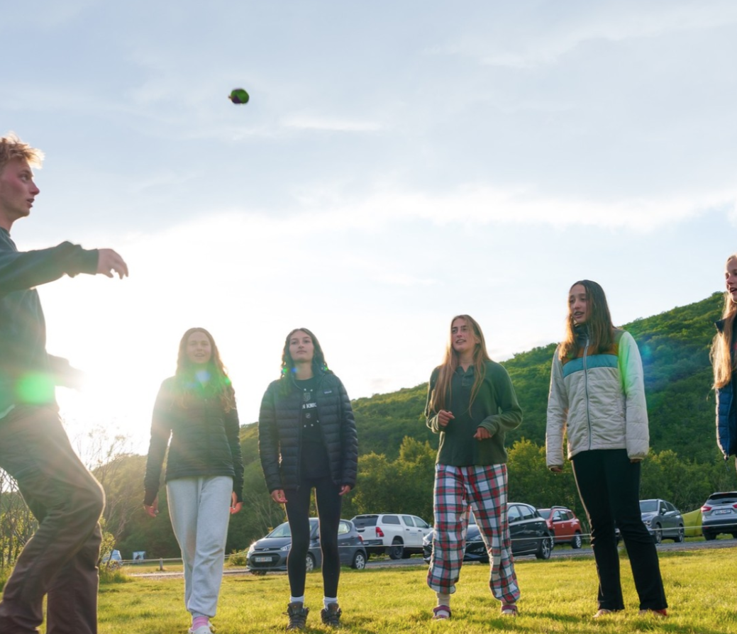 Group of people playing hacky sack outdoors with a clear sky and greenery in the background.